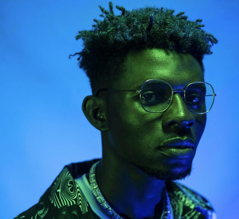 black stereotypes in media and film rarely presented by this image of a black man being a striking portrait of a man with glasses and unique style in neon lighting.